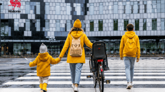 Une maman accompagnée de ses deux enfants traverse un passage piéton à pied et à vélo, illustrant le Challenge piétons et vélos organisé en Wallonie du 16 au 22 septembre.