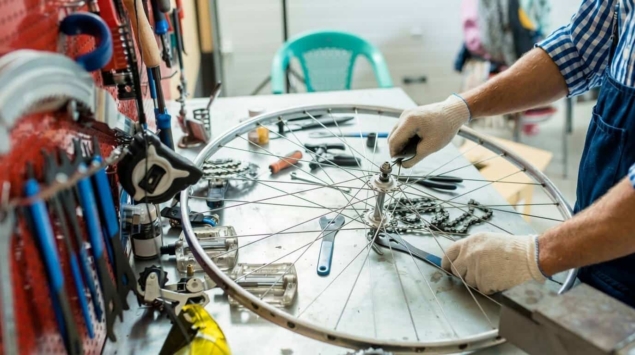 Mains gantées réparant une roue de vélo, entourées d'outils et de pièces mécaniques
