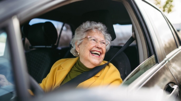 Femme senior souriante au volant de sa voiture, attachée avec sa ceinture de sécurité