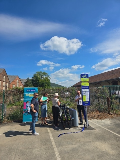 Station de vélos à assistance électrique Vélo Fluo à la gare de Revin, avec panneaux d'information, bornes et vélos disponibles.