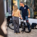 Participants échangeant autour d'un vélo pliant devant un bâtiment vitré.