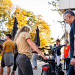 Participante touchant le guidon d'un vélo électrique, entourée d'autres participants.