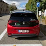 Arrière d’une voiture sombre garée sur un emplacement signalé par un panneau bleu.