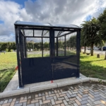 Abri vitré installé sur une pelouse, sous un ciel bleu.